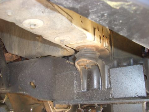 1990 Ford Bronco - Underbody close-up showing a frame crossmember, body mount bushing and floor pan area with surface grime.