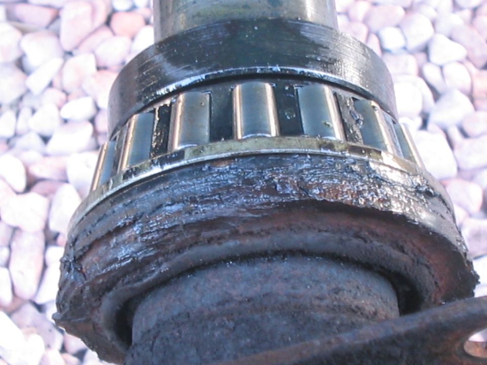 Close-up of a needle roller bearing on a greasy axle shaft journal held over gravel