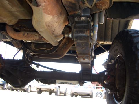 1990 Ford Bronco - Undercarriage detail of a vehicle, showing suspension and drivetrain components. Multiple vehicles in background.