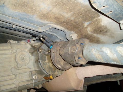 1990 Ford Bronco - Underside view of a drivetrain showing the transfer case or rear axle housing mated to a driveshaft with a U-joint, plus a speed sensor wit…