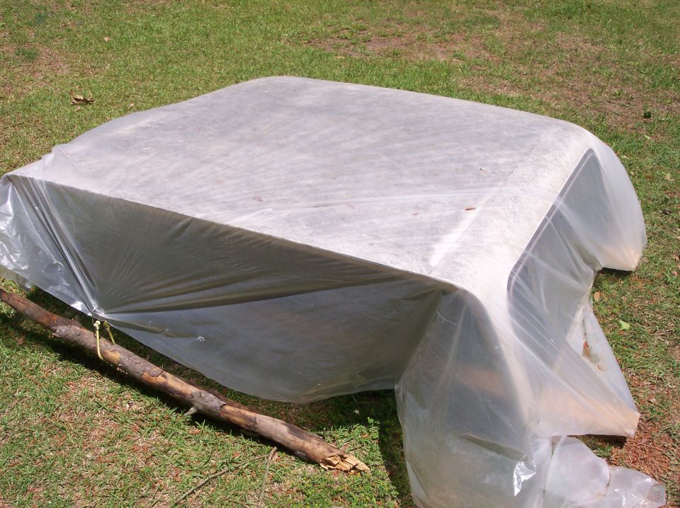 Car hardtop covered with white plastic sheeting and a branch propping it up