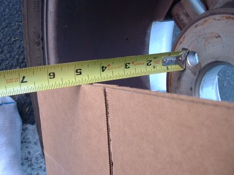 1992 Ford Crown Victoria - A Stanley Life Guard tape measure spans a wheel hub area, measuring backspacing across a brake rotor and hub with lug studs and a lug bolt…