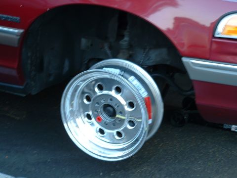 1992 Ford Crown Victoria - A polished aluminum wheel with a machined multi-hole face and mounting labels still attached sits propped against the front wheel well of a…