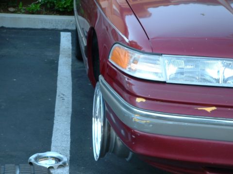 1992 Ford Crown Victoria - Close-up of the right front corner of a maroon sedan parked in a lot, showing the composite headlight with amber turn-signal lens, a two-to…