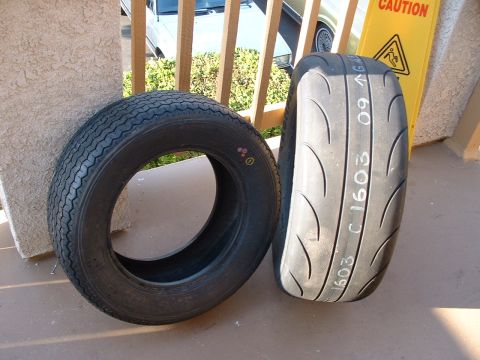 1992 Ford Crown Victoria - Two tires leaned against a stucco wall on a patio: a narrow tall bias-ply-style whitewall-era tire on the left and a wide low-profile direc…