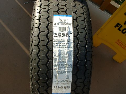 1992 Ford Crown Victoria - Close-up of a new Mickey Thompson Sportsman Front bias-ply tire standing on pavement, its blue-and-white paper label reading "26X8.50-15LT…
