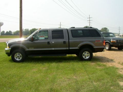 1995 Ford Bronco - A gray Ford F-250 Super Duty truck with a camper shell is parked next to another truck.