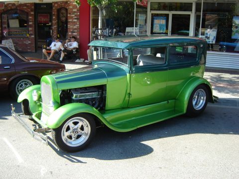 1990 Ford Thunderbird - A custom green sedan hot rod is parked on a street in front of shops.