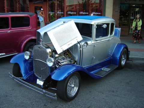 1990 Ford Thunderbird - A classic silver and blue coupe is displayed with its hood open, revealing the engine, while another vintage car sits nearby.