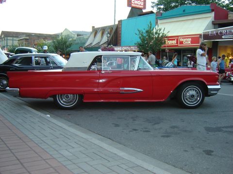 1990 Ford Thunderbird - A classic red convertible with a white top is parked on the street, with other vehicles and buildings in the background.