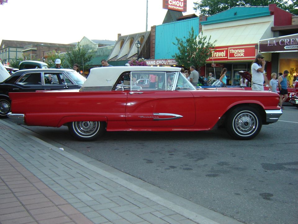 Red convertible with a white top parked on a street, side view