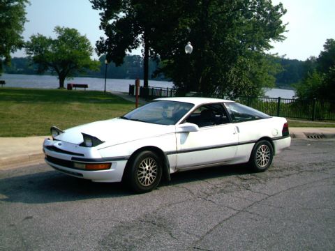 1990 Ford Probe - White 1990 Ford Probe with pop-up headlights parked near a body of water on a sunny day.