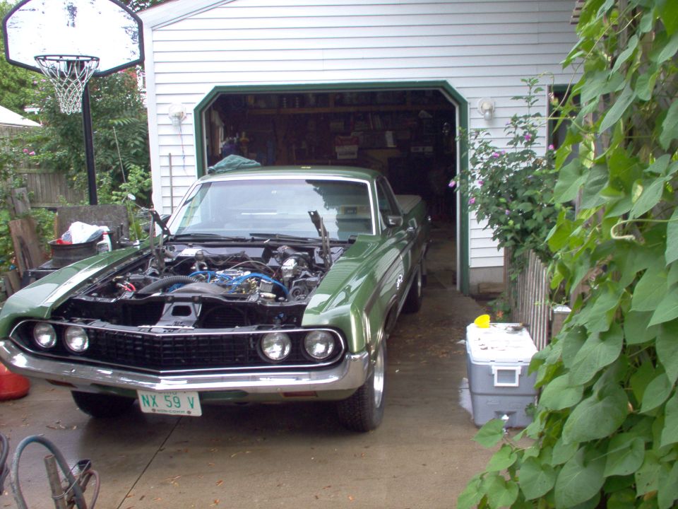 Green 1970s Ford Ranchero with hood up in driveway by open garage