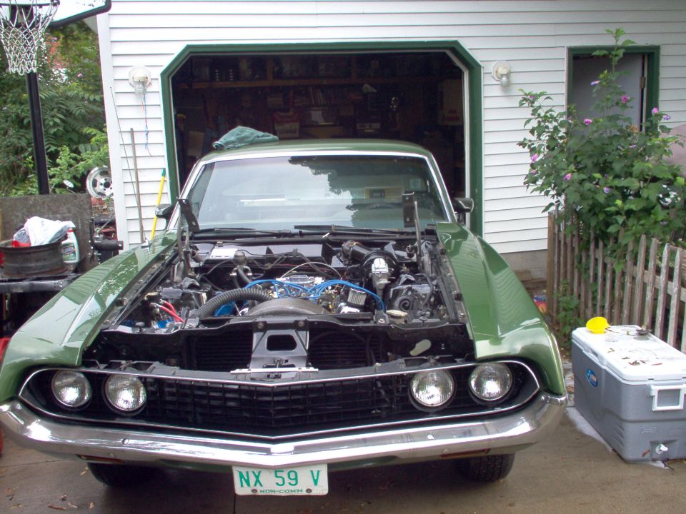 Light green Ford Ranchero with hood up showing blue V8 engine, front view