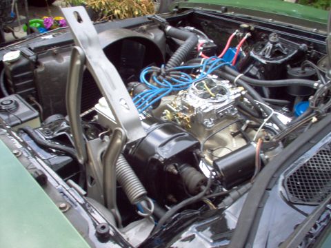 1970 Ford Ranchero - The engine bay of a green 1970 Ford Ranchero features a chrome carburetor and bright blue spark plug wires.
