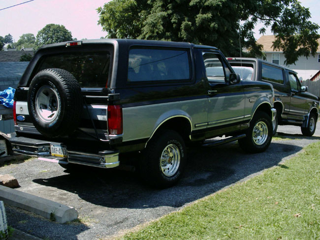 Rear view of two-tone black and silver Ford Broncos on a trailer in a residential driveway