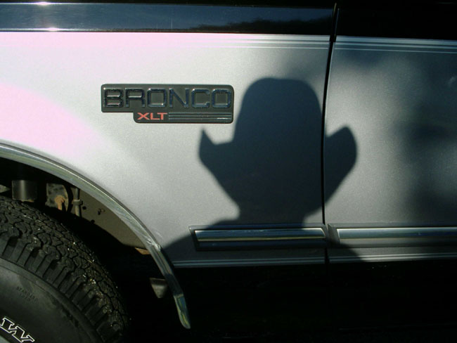 Silver Bronco XLT door emblem with a cowboy-hat shadow cast across the body panel