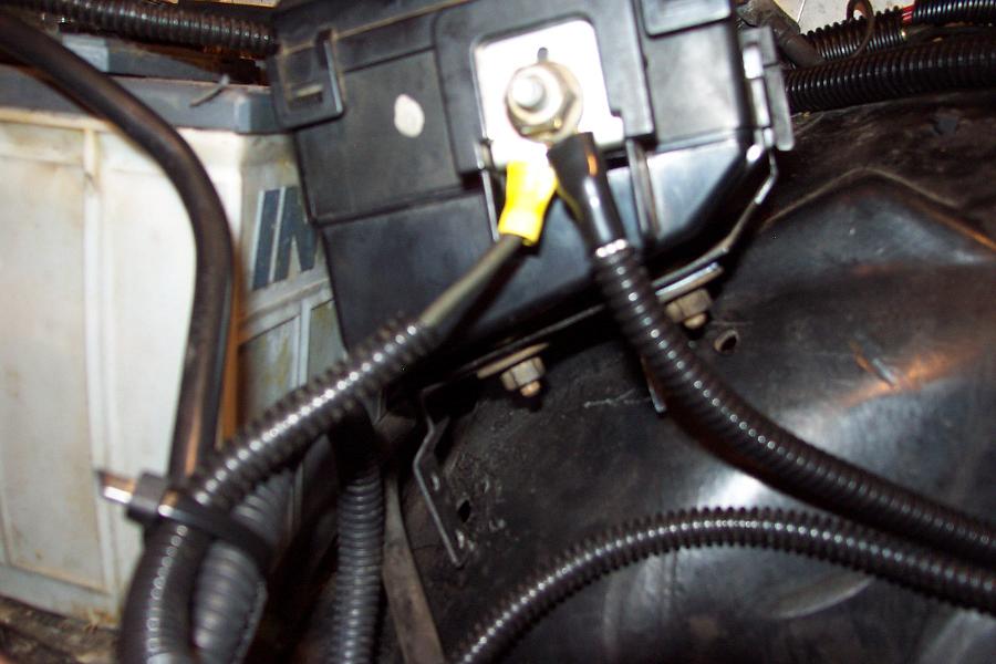Close-up of a car battery terminal with yellow-capped wire and black protective tubing