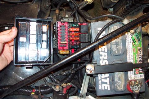 1985 Ford Crown Victoria LTD - Close-up view of a vehicle's fuse box and battery, with a hand holding an open fuse box cover.