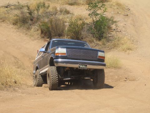 1990 Ford Bronco - black lifted Ford Bronco with a billet grille crests a dirt embankment off-road, front wheels lifting over the lip.