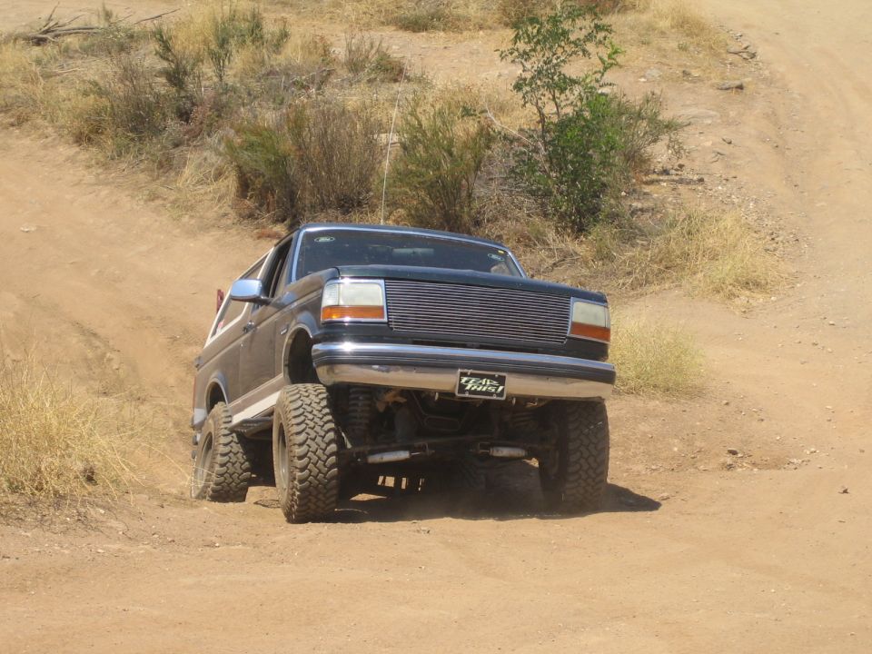Black lifted Ford Bronco with chrome grille climbing a dirt embankment