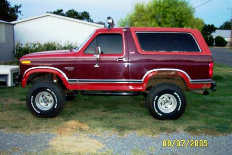 1982 Ford Bronco - Side view of a lifted maroon Ford Bronco with red trim and aftermarket wheels.