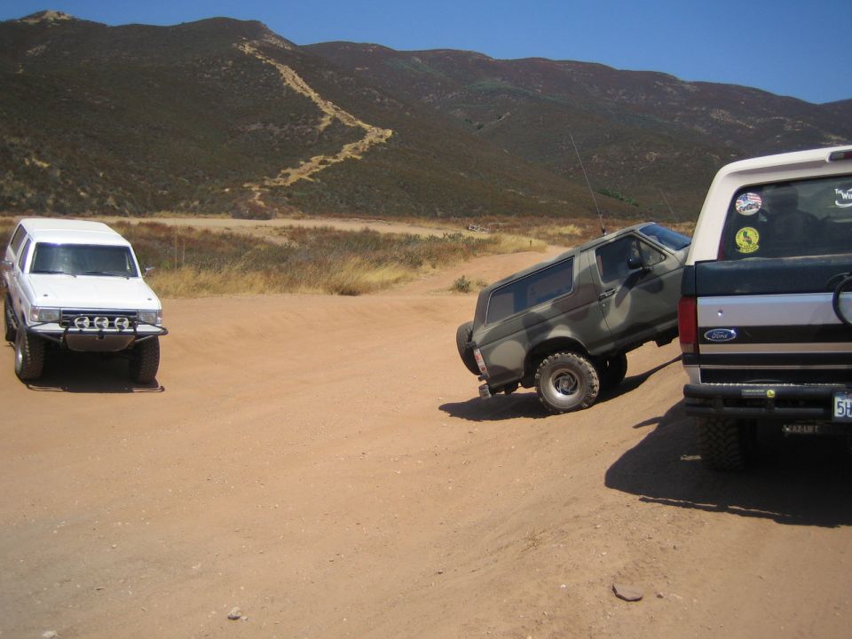 White SUV and camo truck off-road near the tailgate of a black Ford pickup