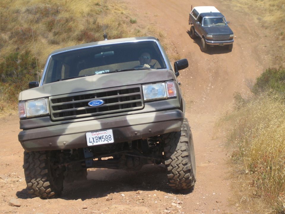Camouflage lifted Ford truck on a dirt trail with a second SUV behind it