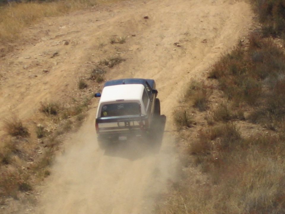 Rear of a white-topped SUV kicking up dust while driving up a dirt trail
