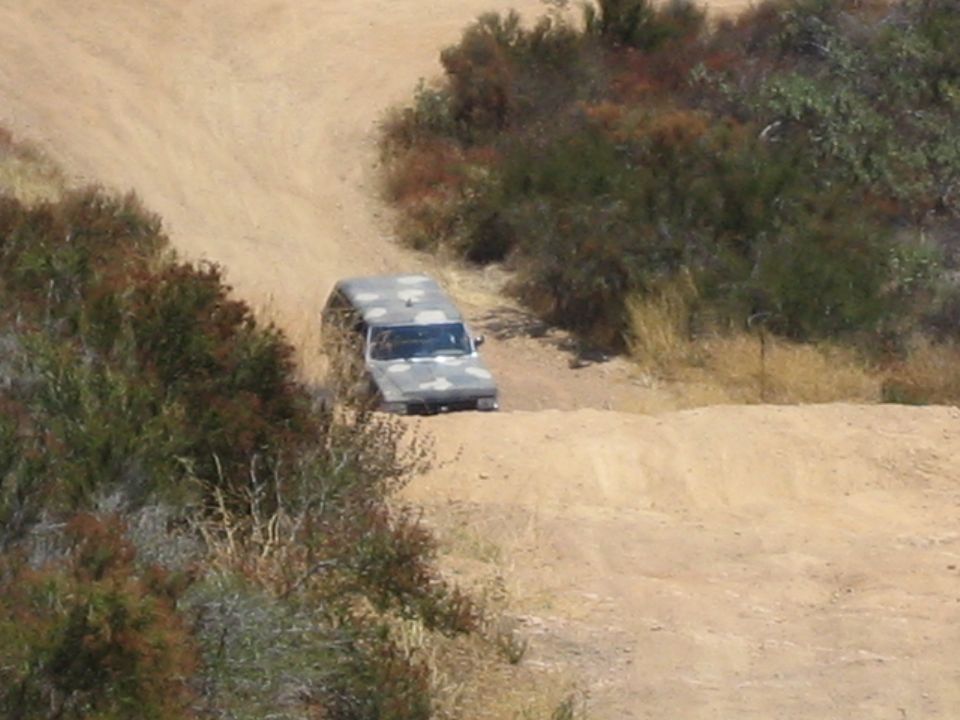 Camouflage truck driving along a dirt trail between brushy banks