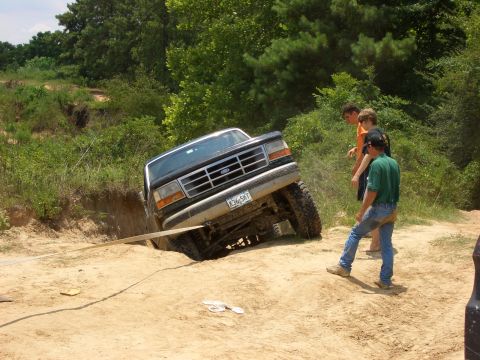 1990 Ford Bronco - A Ford truck is stuck in a ditch, with a tow strap attached, while onlookers observe the situation.