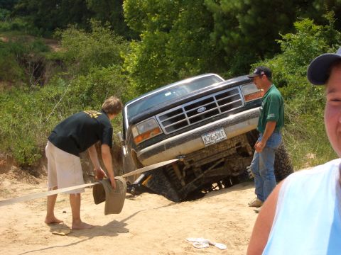 1990 Ford Bronco - A black Ford F-Series truck is stuck on a dirt incline, with two men nearby trying to help it.