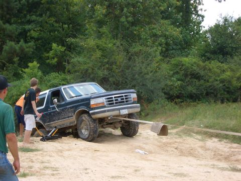 1990 Ford Bronco - A dark green 1990 Ford Bronco is being pulled out of a sandy ditch by a strap as people watch.