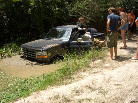 1990 Ford Bronco - A black pickup truck is stuck in the mud with people standing around it.