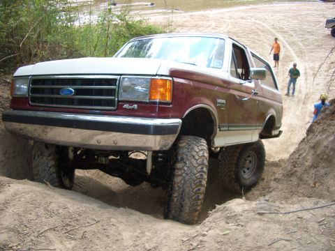 1990 Ford Bronco - This lifted Ford Bronco navigates a challenging off-road trail with onlookers present.