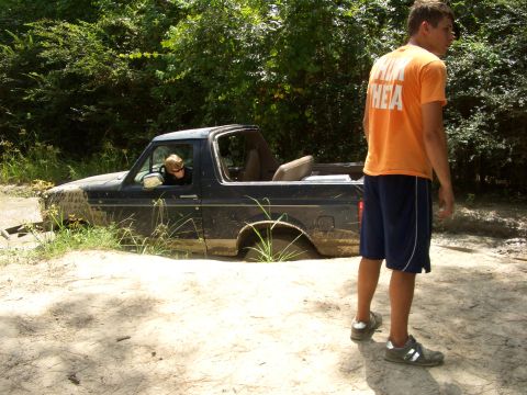 1990 Ford Bronco - A 1990 Ford Bronco is stuck deep in the mud with a person in the driver's seat and another person standing nearby.