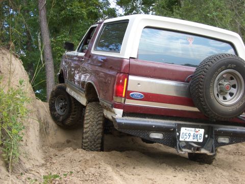 1990 Ford Bronco - A 1990 Ford Bronco navigates a steep dirt path, its rear tire digging into the loose soil.