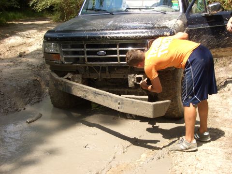 1990 Ford Bronco - A person inspects the front of a mud-covered 1990 Ford Bronco that is stuck in a muddy ditch.