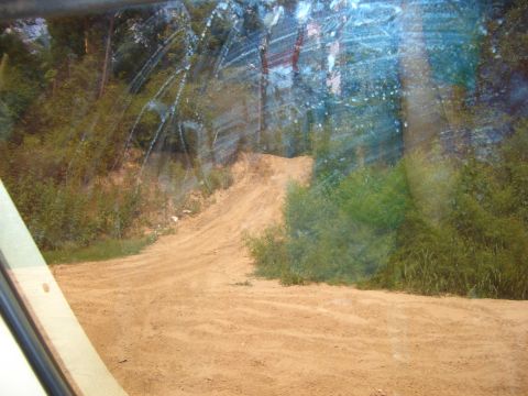 1990 Ford Bronco - View from inside a vehicle looking out at a sandy hill with vegetation and trees in the background.