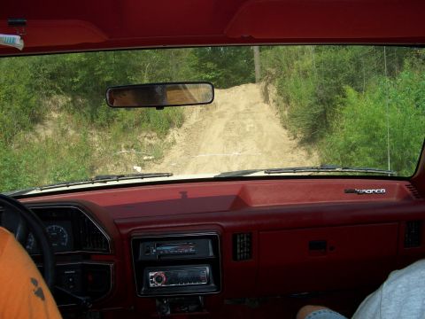 1990 Ford Bronco - Interior view of a Ford Bronco navigating a rough dirt path through a wooded area.