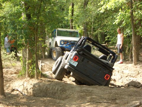 1990 Ford Bronco - Two off-road vehicles navigate a challenging dirt trail with trees on either side.