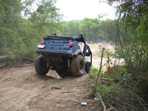 1990 Ford Bronco - An off-road vehicle navigates a challenging dirt trail, with other vehicles visible in the background.