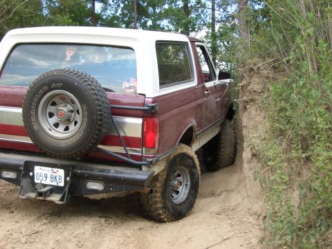 1990 Ford Bronco - Ford Bronco navigating a tight dirt trail with steep embankment.