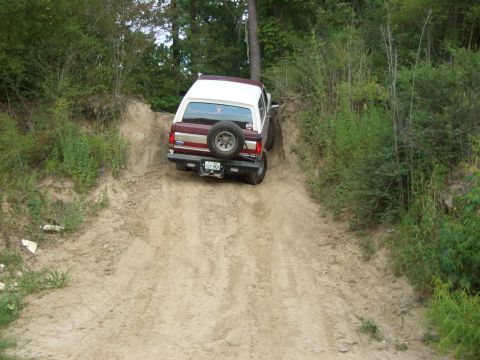 1990 Ford Bronco - A Ford Bronco navigates a steep, sandy incline surrounded by dense foliage.