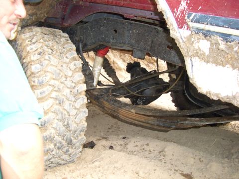 1990 Ford Bronco - The undercarriage of a red 1990 Ford Bronco shows its suspension system and a large, mud-covered tire.