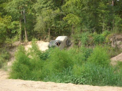 1990 Ford Bronco - A white 1990 Ford Bronco is seen tilted on its side in a ditch, surrounded by dense foliage.
