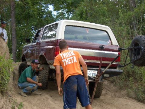 1990 Ford Bronco - A group works on a Ford Bronco stuck on a dirt trail, with a spare tire mounted on the back.