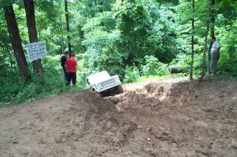 1988 Ford Bronco - White SUV stuck in mud on a wooded trail, with two people observing.