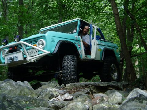 1969 Ford Bronco - A teal Ford Bronco navigates a rocky trail, its driver visible behind the wheel.