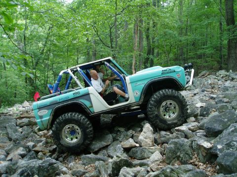 1969 Ford Bronco - A modified 1969 Ford Bronco navigates a challenging rocky obstacle course in a forest setting.